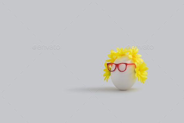 Close up of an egg wearing a wig and sunglasses sitting in front of a plain wall backdrop