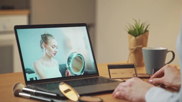 Young Woman Learn How to Apply Makeup While Watching a Female Beauty Blogger's Lesson on a Laptop alt