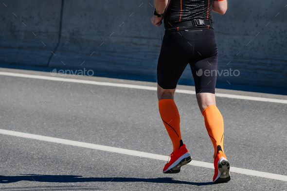 side view male athlete in compression socks running marathon race on road, summer sports event
