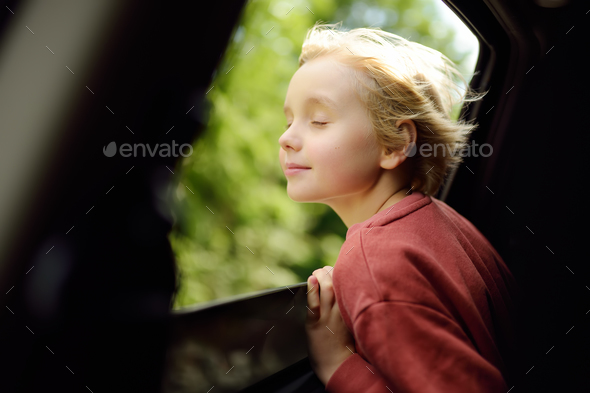 Cute preteen boy inhales the air of freedom from car window during family road trip