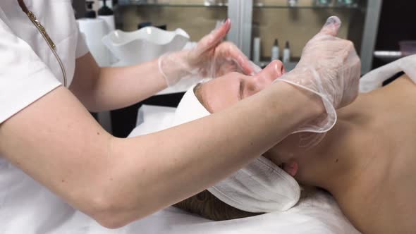 A Female Cosmetologist Cleanses a Client's Face with Foam in a Beauty Salon