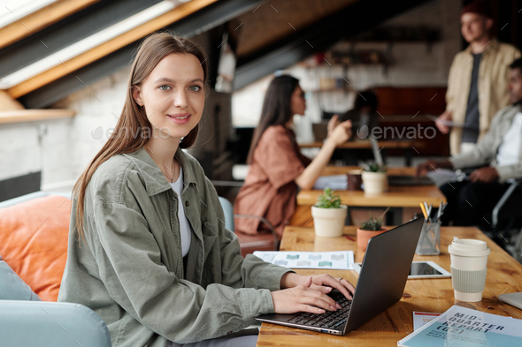 Young smiling female analyst or economist looking at camera by workplace