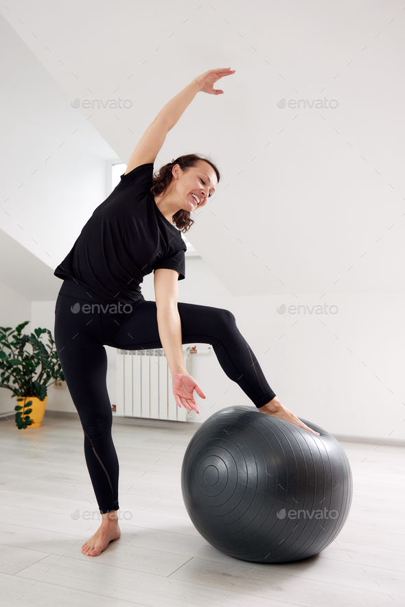 A young girl is doing Pilates on a reformer bed in a bright studio. A  beautiful slender brunette in Stock Photo by Gerain0812