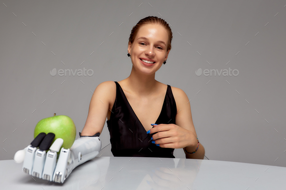 Young girl with disability wearing sensory bionic prosthetic arm seats at the table in studio