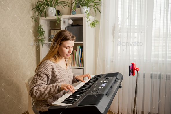 Woman learns music, playing piano online at home interior.