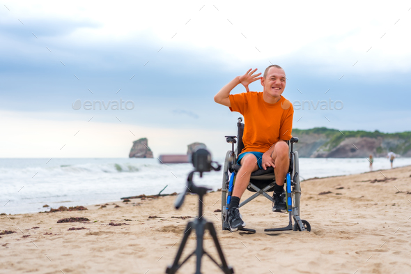 Portrait of a disabled person in a wheelchair on the beach recording a video clip