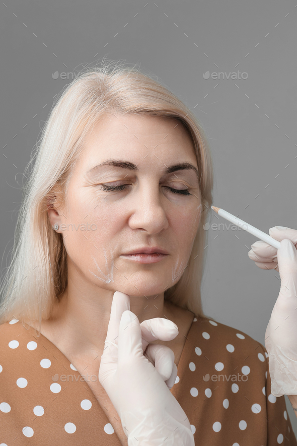 The beautician makes markings on the woman's face with a white pencil