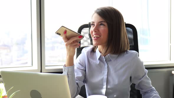 Confident businesswoman holding smartphone near mouth for recording voice message alt