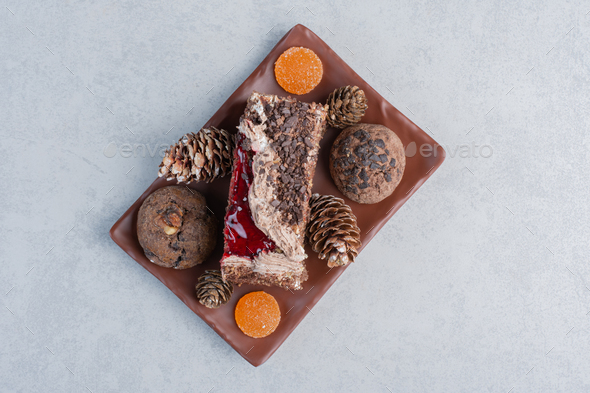 Cookies, pine cones, marmelades and a slice of cake on a platter on marble background