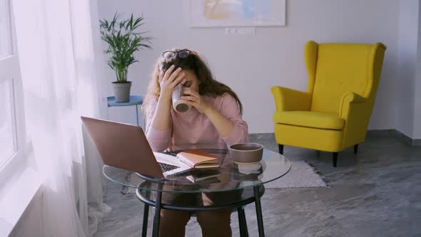 Tired Woman Has Breakfast Trying to Work on Laptop at Table