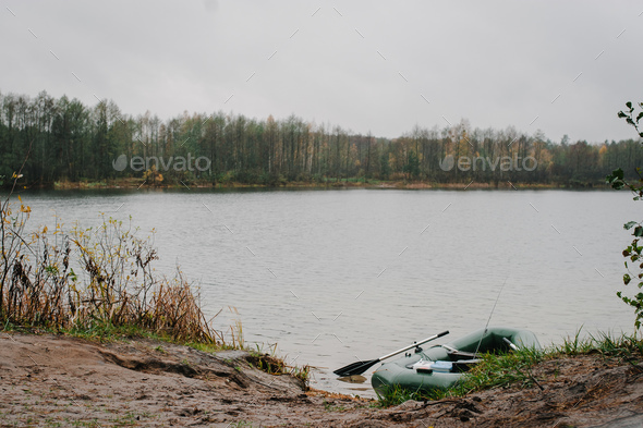 An inflatable boat, with boxes with fishing tackles, is standing on the water, pond, lake, near