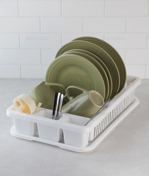 A plastic dish drying rack in the kitchen with clean dishes inside.