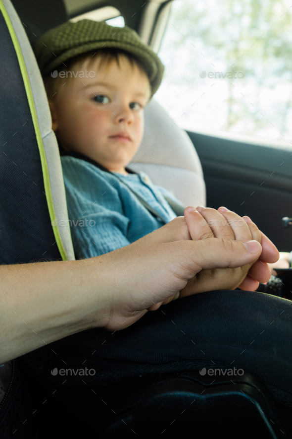 Child safety during car trip. Mother hand holding toddler boy sitting