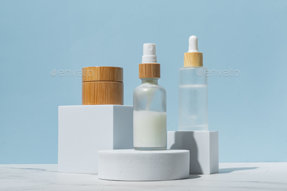 Set of beauty products in glass and bamboo bottles on white podiums on blue background. Skincare set