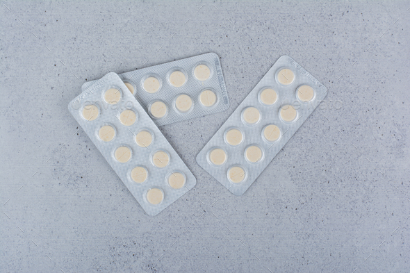Three packs of round medicine pills on marble background