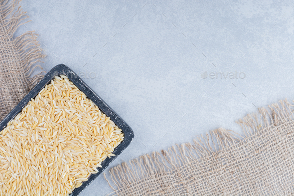 Brown rice on a worn-out black tray on marble background