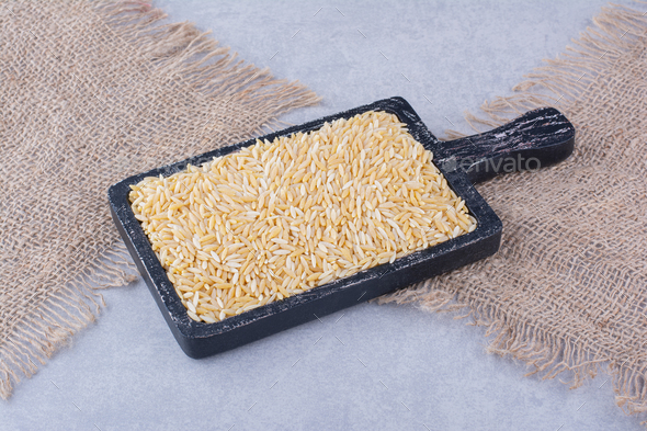 Worn-out black tray stocked with brown rice on marble background