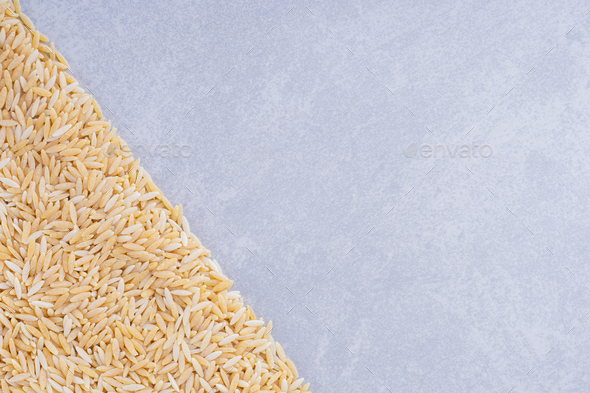 Heap of brown rice arranged in a triangle shape on marble background