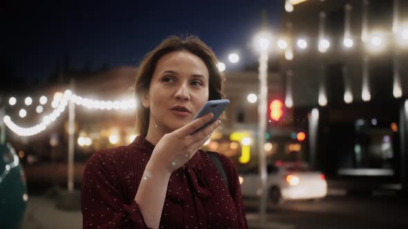 Happy woman using a smart phone voice recognition function online walking on a city street. alt