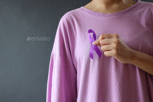 Close up hand holds purple ribbon on purple t shirt support cancer awareness