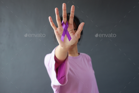 Woman in purple t-shirt holding showing purple awareness ribbon on palm, covering face