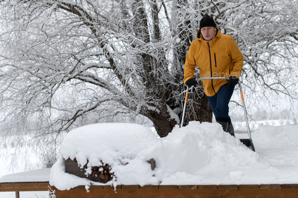 Portrait of a man in winter clothes with snow shovel cleaning snow from the  terrace of the building Stock Photo by zelmab