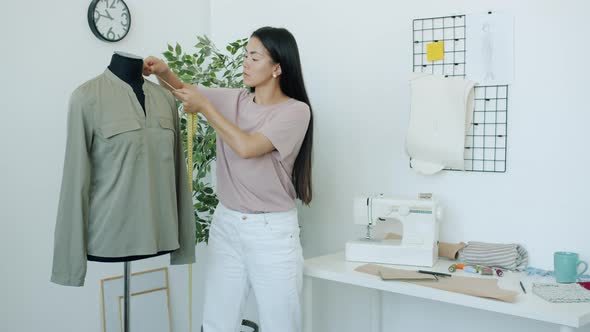 Serious Asian Fashion Designer Measuring Garment on Tailor's Dummy Busy with Creative Work in Studio alt