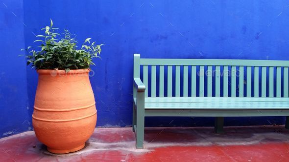 Green bench and pot sitting outside a blue wall next to a large planter