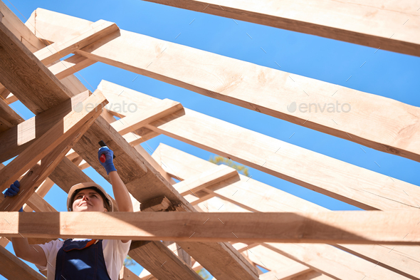 Woman general contractor hammering nail into wooden frame of roof construction
