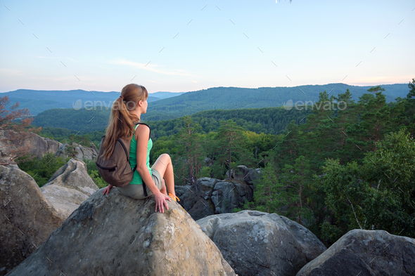 Hiker girl resting on rocky mountain top enjoying morning nature during her travel