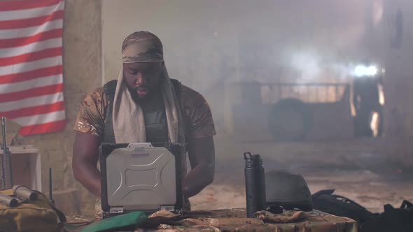 Black Military Man Using Laptop and Radio at Base alt