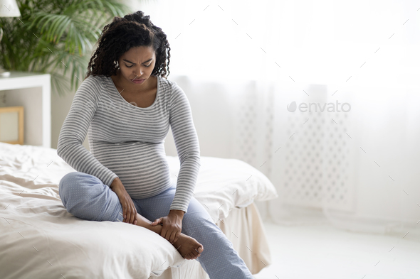 Health Problems During Pregnancy. Black pregnant woman in homewear massaging swollen foot