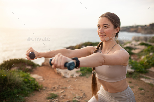 Positive young european woman athlete in sportswear make arm exercise with  dumbbells, squat Stock Photo by Prostock-studio