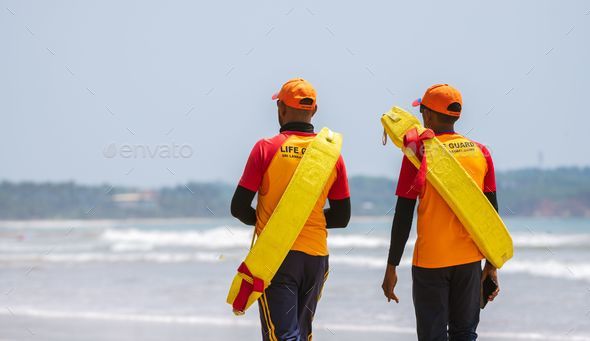 Two Lifeguards on duty at the tropical beach, Both carrying rescue tubes on their shoulders