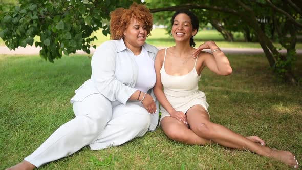 Lovely Beautiful Happy Lesbian African American Couple Sitting on Green Grass Hugging Outside at