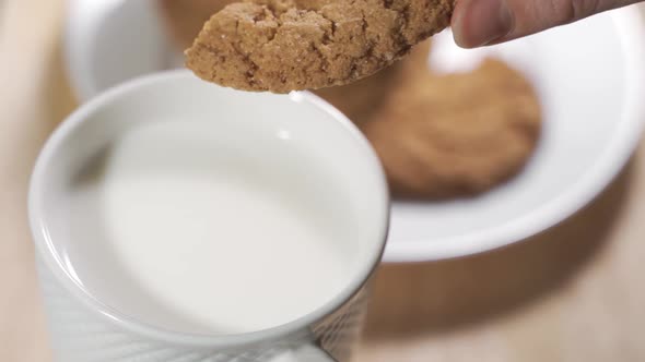 A Woman Hand Dunks a Cookie in the Milk Mug During the Breakfast in a Warm Morning. alt