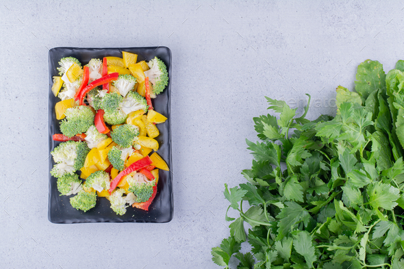 Dietary salad mix on a black platter next to parsley bundle on marble background