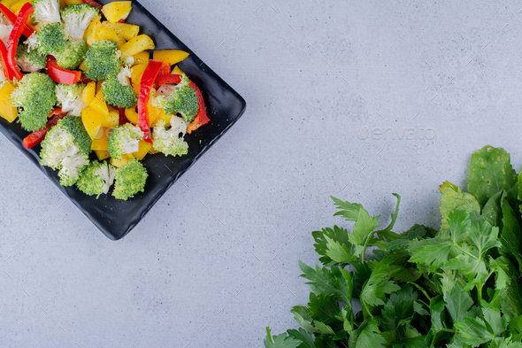 Healthy salad mix on a black platter next to parsley bundle on marble background