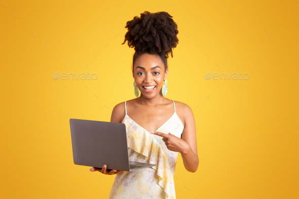 Cheerful young black woman pointing finger at laptop, recommending social media app