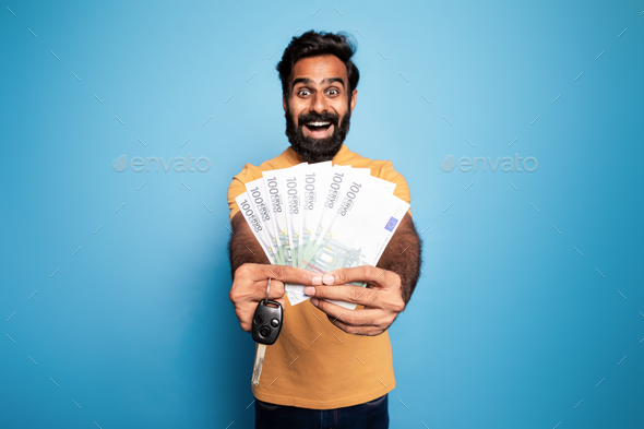 Make dream come true. Portrait happy indian man showing new car key and money cash dollars in hand