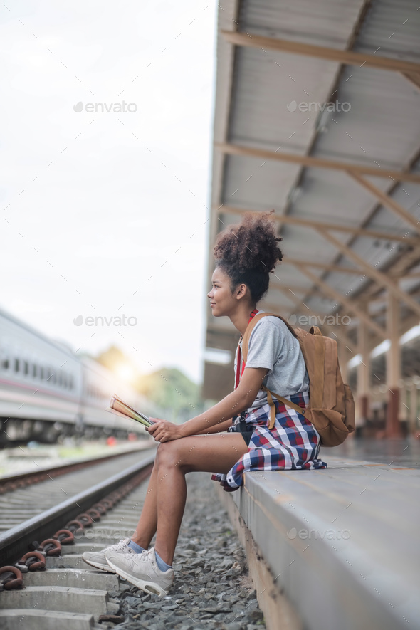 Young woman female smiling traveler with back pack looking to map while waiting for the train at