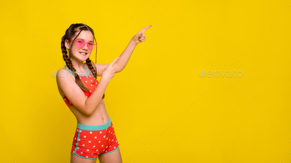 girl in swimsuit points with her index finger to free copyspace for advertising on yellow background