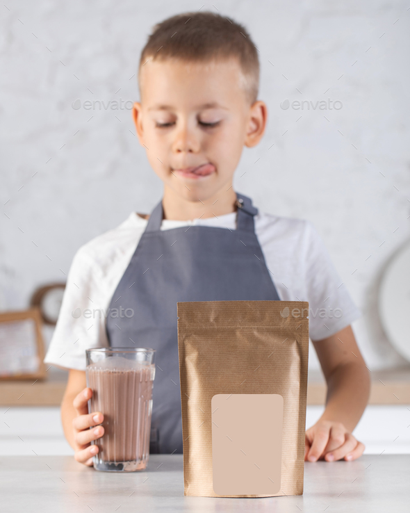 A cute joyful boy holds a glass of cocoa and a craft package with a place for a logo.