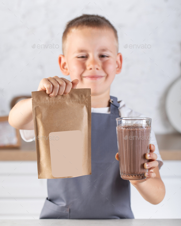 A cute joyful boy holds a glass of cocoa and a craft package with a place for a logo.