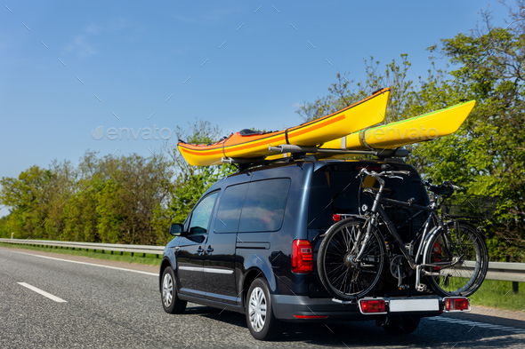 Back view modern black family wagon van car with mounted roof kayak and bike tail carrier driving