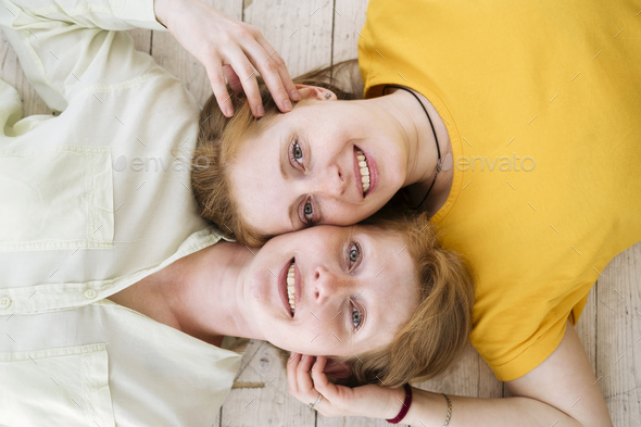 Two red-haired sisters lie cheek to cheek and smile. Similar women with fair skin and freckles.