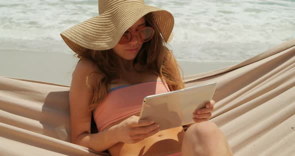 Front view of Caucasian woman using digital tablet in a hammock at beach 4k alt