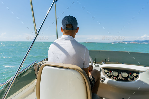 Bach view of middle-aged man driving luxury motor yacht. Captain at the helm of motor boat.