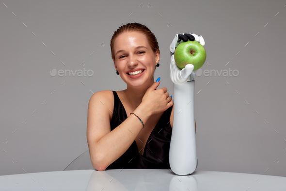 Young smiling girl with disability wearing sensory bionic prosthetic arm seats at the table