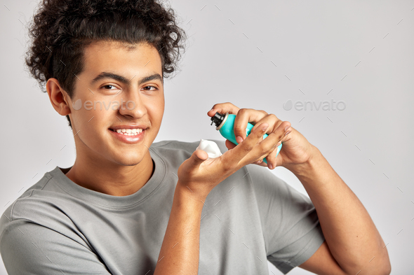 Happy young smiling guy putting facial wash on his fingers, preparing to apply the beauty product on